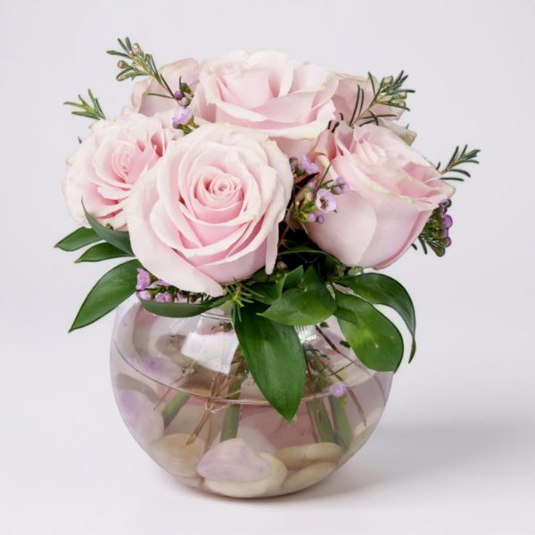 Blush pink rose arrangement in round glass vase with greenery and waxflower