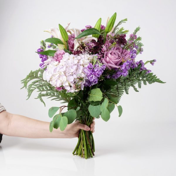 Lavender and purple bouquet with roses, hydrangea, lilies, and greenery held in hand