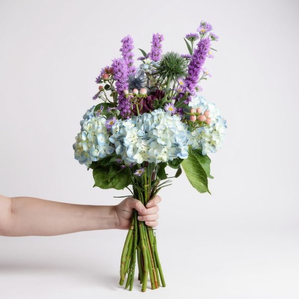 Handheld bouquet with blue hydrangeas, purple liatris, thistle, and berry accents