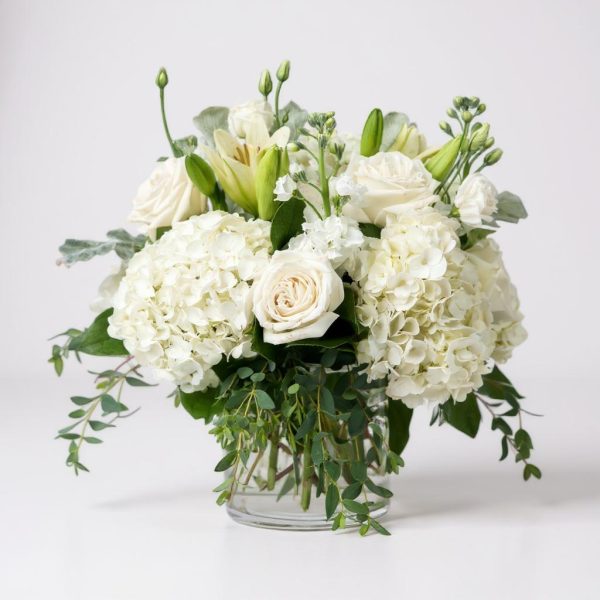 All white flower arrangement with hydrangeas, roses, lilies, and eucalyptus in a glass vase
