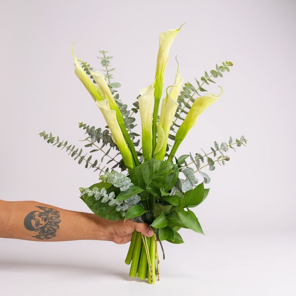 Hand holding bouquet of white calla lilies with silver eucalyptus and green foliage