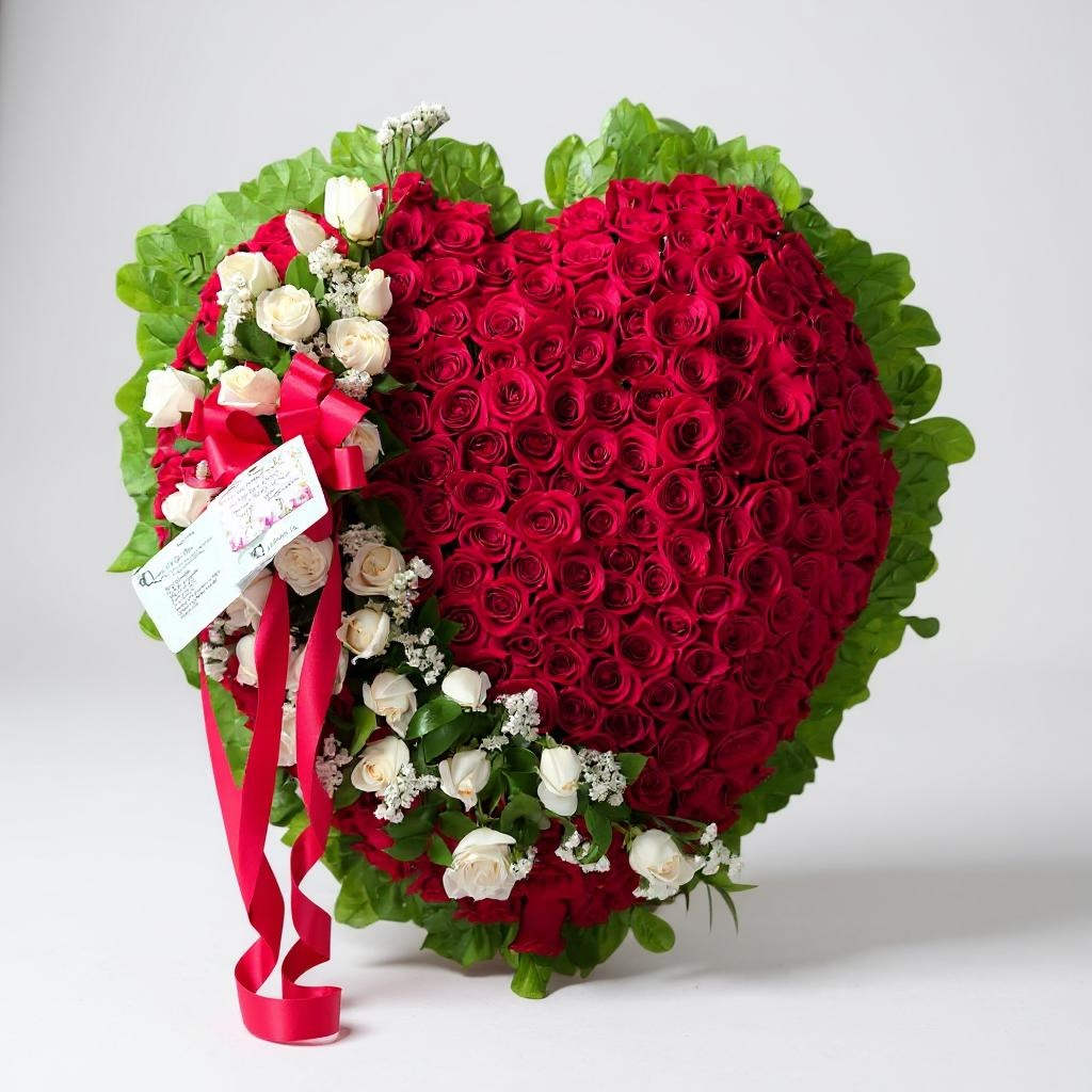 Funeral heart spray with red roses, white roses, greenery, and red ribbon bow