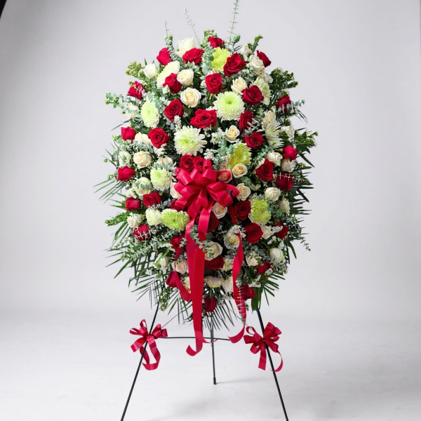 Funeral standing spray with red roses, white roses, chrysanthemums, greenery, and red ribbon bow on easel