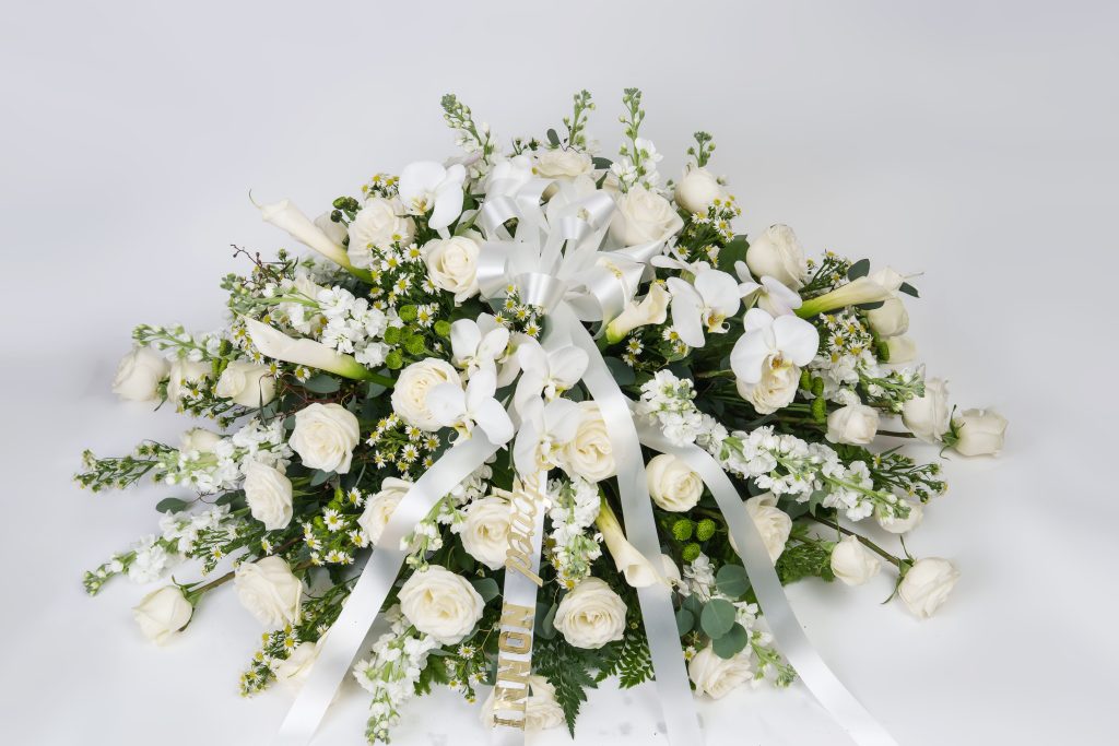 White casket spray with roses, orchids, lilies, stock, greenery, and satin white ribbons