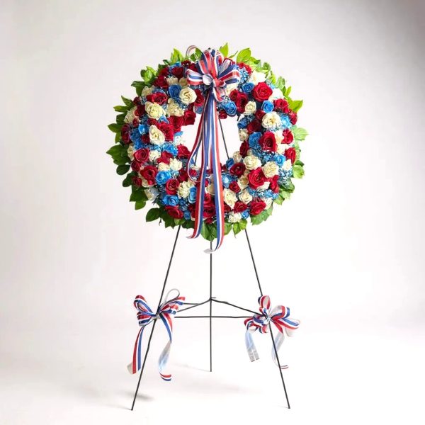 Funeral wreath with red, white, and blue roses, greenery, and patriotic ribbon on easel