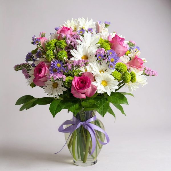sweet harmony flower arrangement with pink roses, daisies, and lavender asters in clear glass vase with lilac ribbon