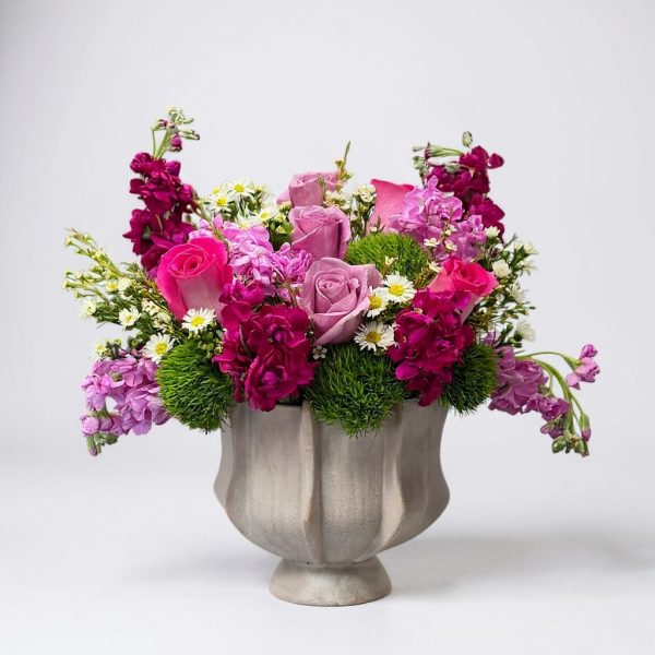 Pink and purple flower arrangement in pedestal vase with roses, stock, dianthus, and daisies