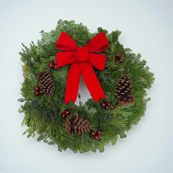 Christmas wreath with red velvet bow, pinecones, and red berries on fresh evergreen foliage