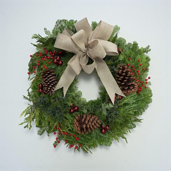 Christmas wreath with linen bow, red berries, pinecones, and fresh evergreen foliage.