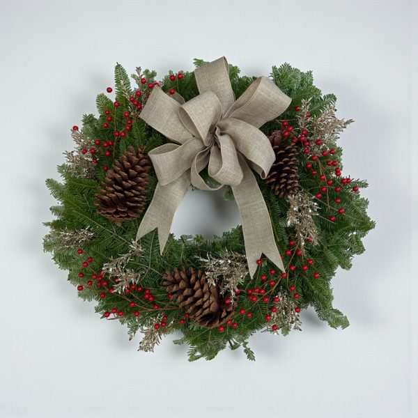 Christmas wreath with linen bow, gold foliage, red berries, pinecones, and fresh evergreen branches.