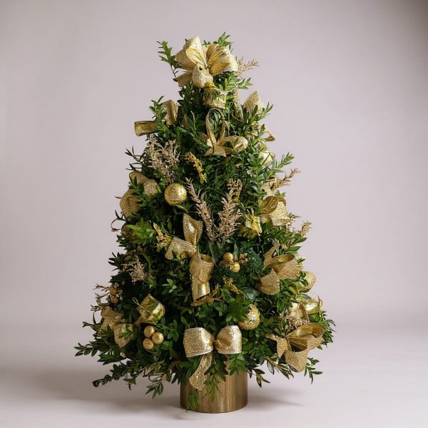 Decorated boxwood Christmas tree with gold ribbon and holiday accents in decorative container