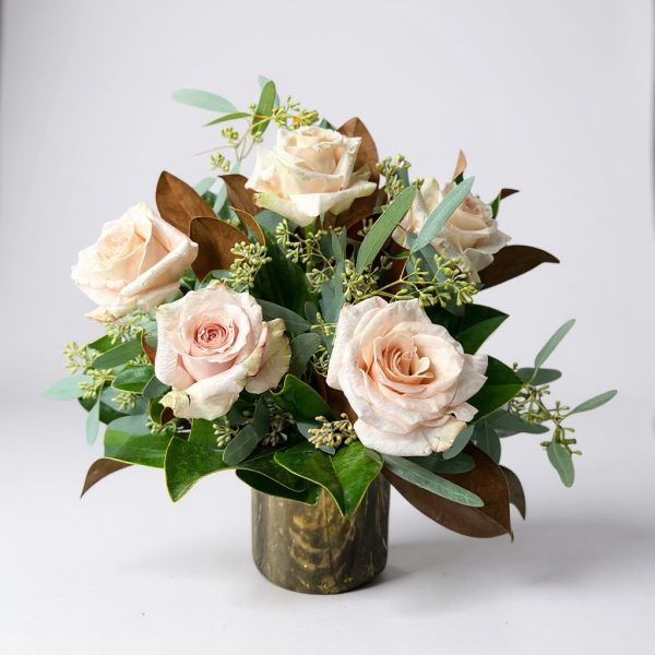 Arrangement of blush champagne roses with greenery and magnolia leaves in a metallic vase