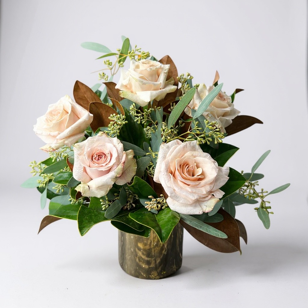 Arrangement of blush champagne roses with greenery and magnolia leaves in a metallic vase