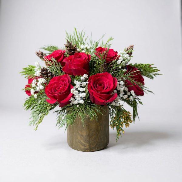 Christmas arrangement with red roses, winter greenery, white accents, and pinecones in a holiday vase