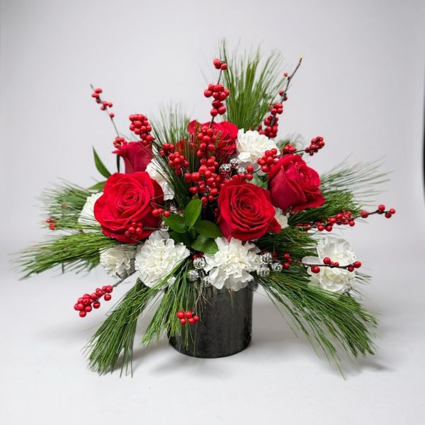 Christmas flower arrangement with red roses, white carnations, red berries, pine greenery, and holiday accents