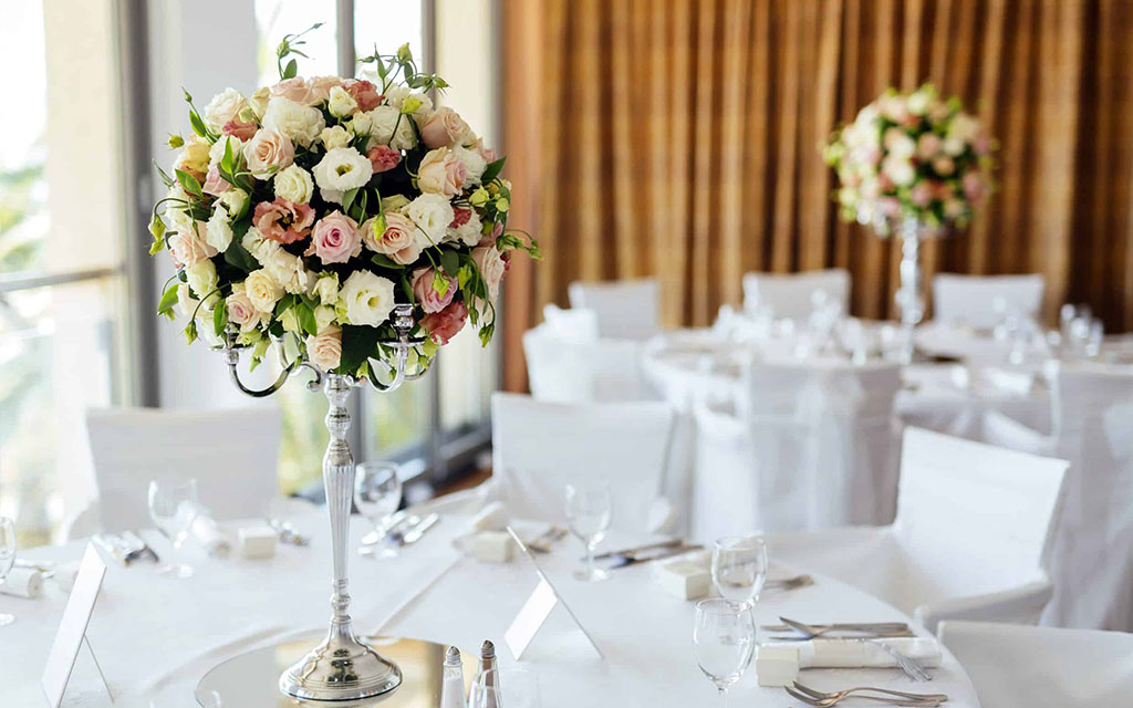 Elegant seasonal wedding flowers centerpiece with blush and cream roses on tall silver stand at formal reception table