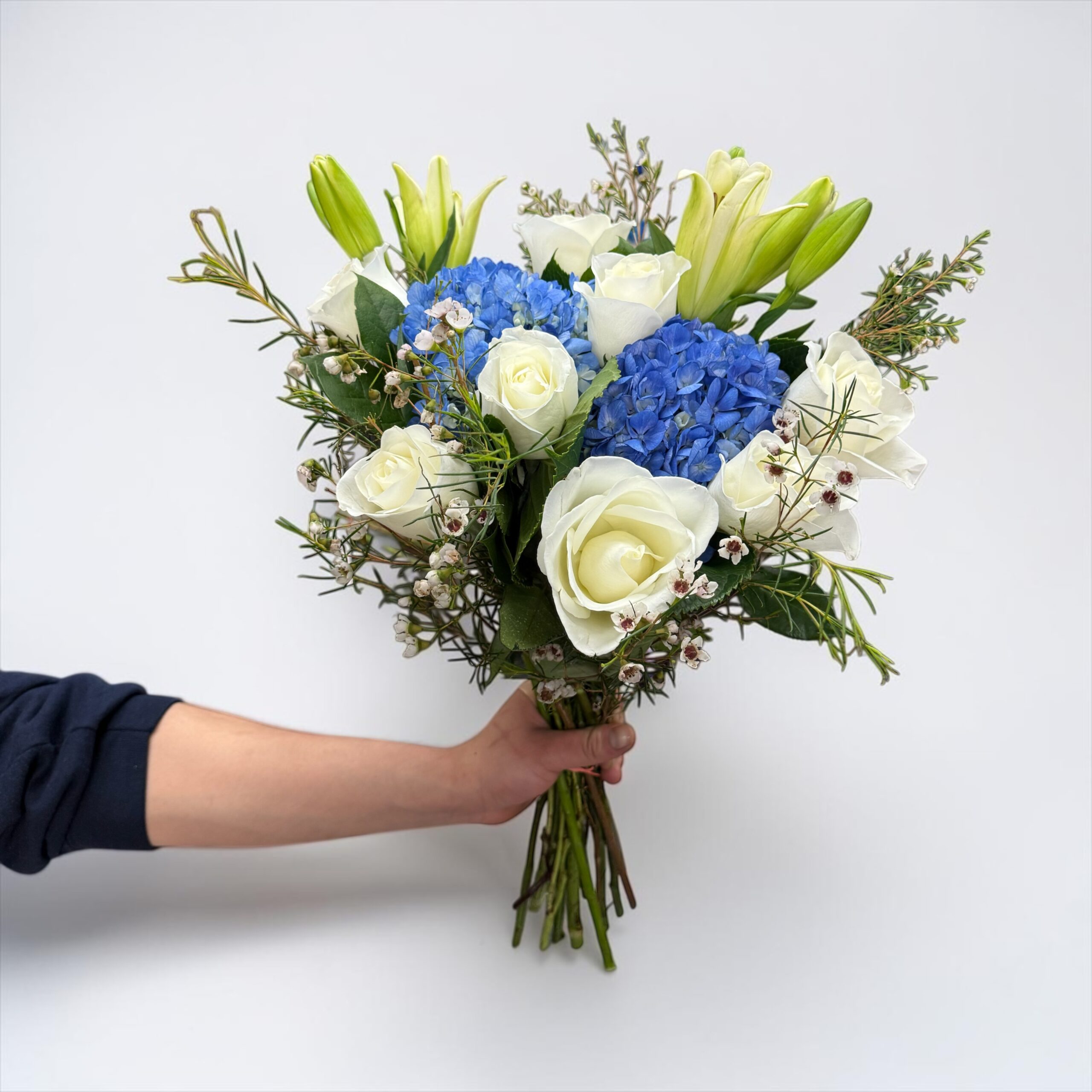 Blue hydrangea bouquet with white roses, lily buds, waxflower, and fresh greenery hand-tied by Quinn Florist