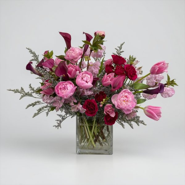 Pink peonies, burgundy calla lilies, tulips, and red spray roses in a clear glass cube vase