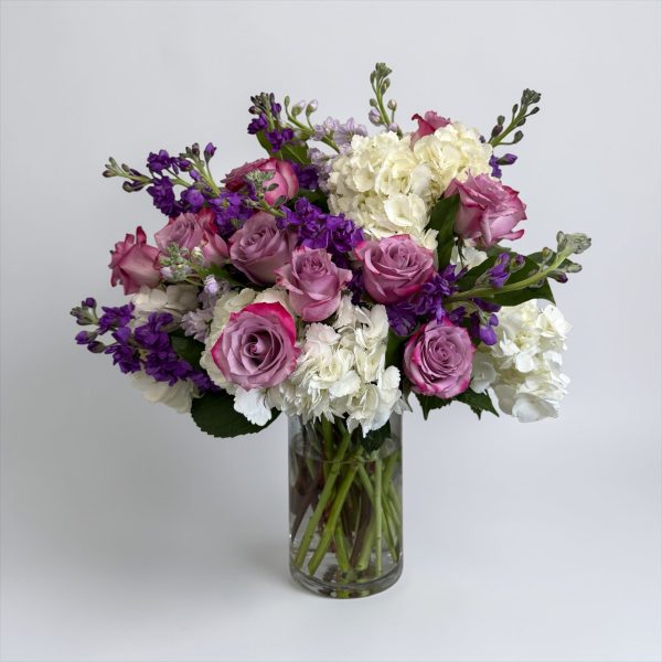 Lavender roses, white hydrangeas, and purple stock arrangement in a clear glass vase