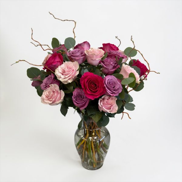 Pink, blush, lavender, and fuchsia rose arrangement with eucalyptus in a clear glass vase