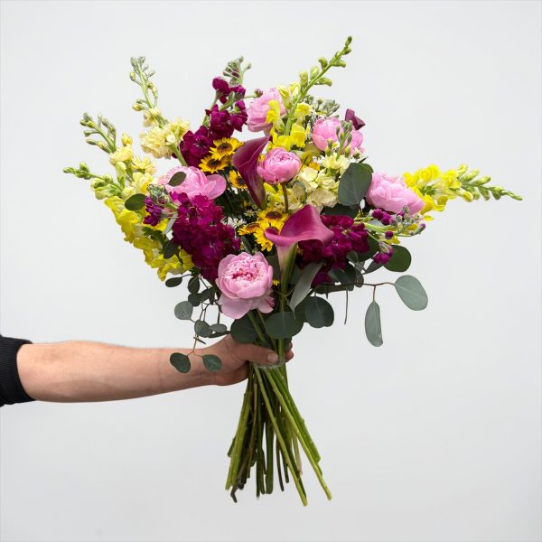 Hand-tied bouquet with pink peonies, burgundy calla lilies, yellow snapdragons, magenta stock, and seasonal blooms