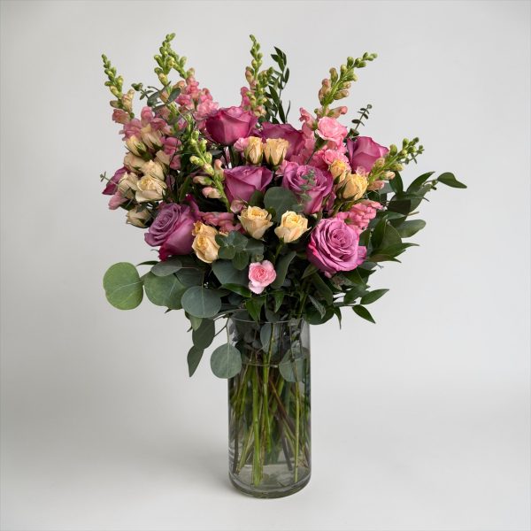 Pink and lavender roses with blush snapdragons, cream spray roses, and eucalyptus in a clear glass vase