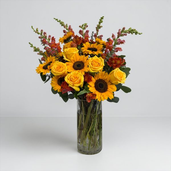 Sunflowers, yellow roses, and orange seasonal blooms in a clear glass vase