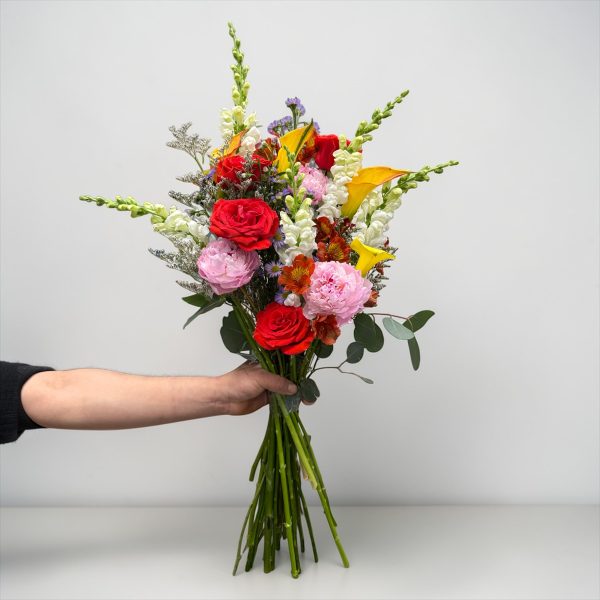Hand-tied bouquet with red roses, pink peonies, yellow calla lilies, white snapdragons, and seasonal accents