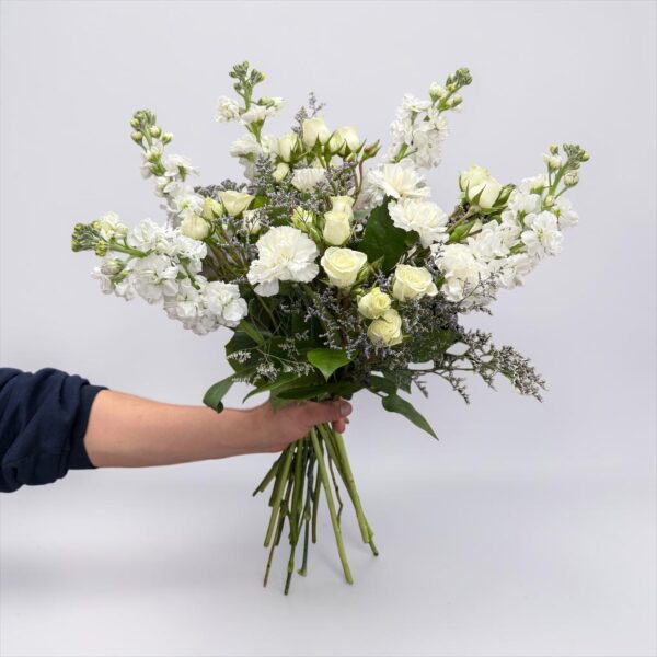 White rose bouquet with white stock, white carnations, delicate filler flower, and fresh greenery hand-tied by Quinn Florist