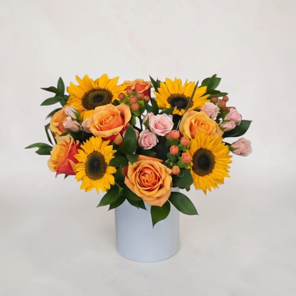 Sunflower and peach rose arrangement with pink spray roses in a white vase