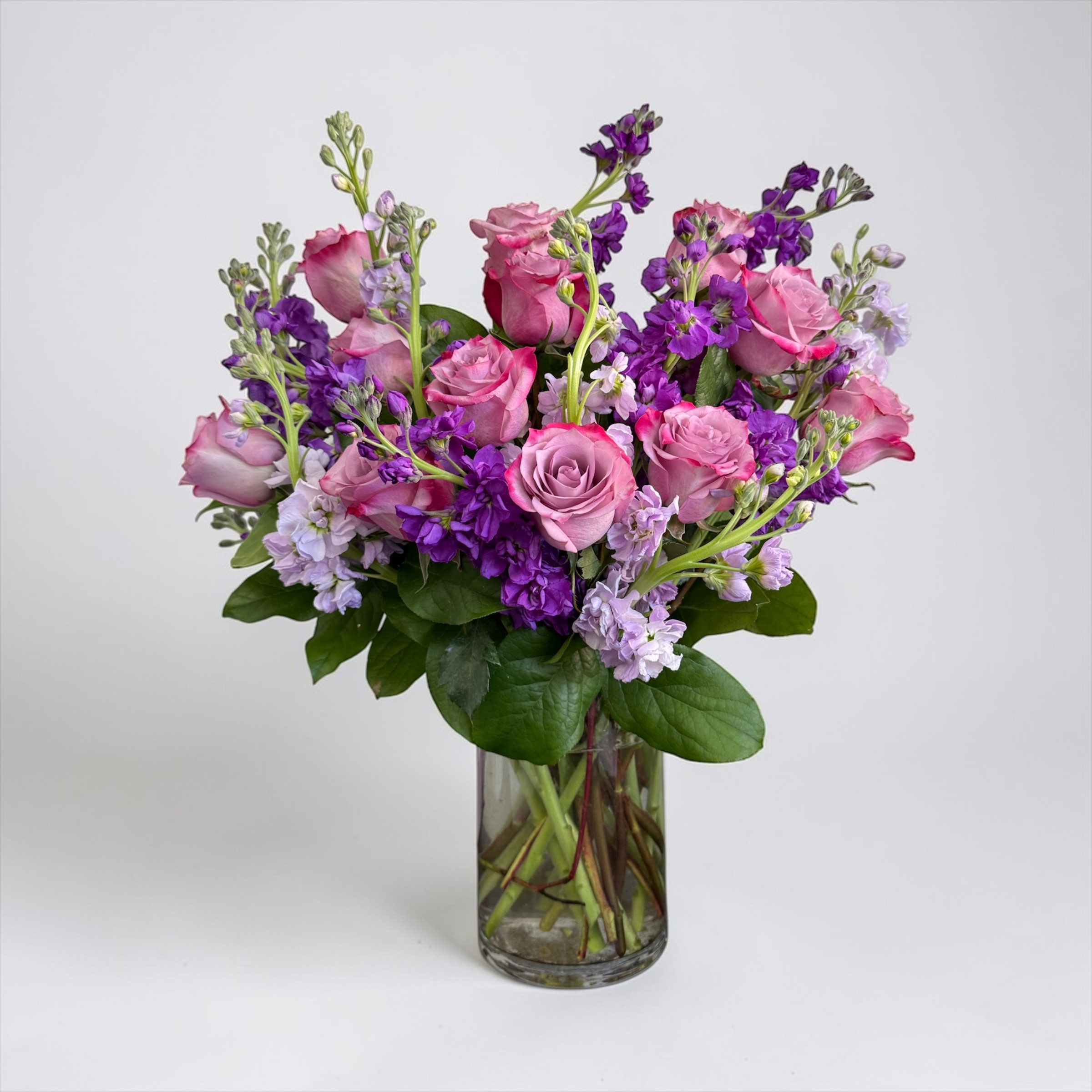 Pink and lavender rose arrangement with purple stock in a clear glass vase
