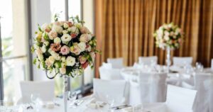 Wedding flowers on a reception table: a tall centerpiece of blush roses and lisianthus on a silver stand