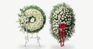 A white funeral wreath and a white rose standing spray from Quinn Florist, each on its easel